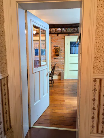 Interior passage with a paneled door featuring glass inserts, wood-finish flooring, exposed brick wall, and decorative wallpaper