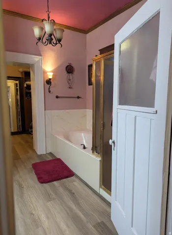 Master bathroom featuring a built-in tub with a shower enclosure, wood-finish flooring, wall sconces, and an overhead chandelier
