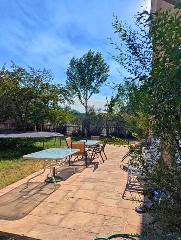 Expansive patio area featuring large format paver stones, a perimeter of mature landscaping, and an adjacent lawn space