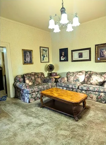 Living area featuring textured wallpaper, crown molding, and a five-light chandelier