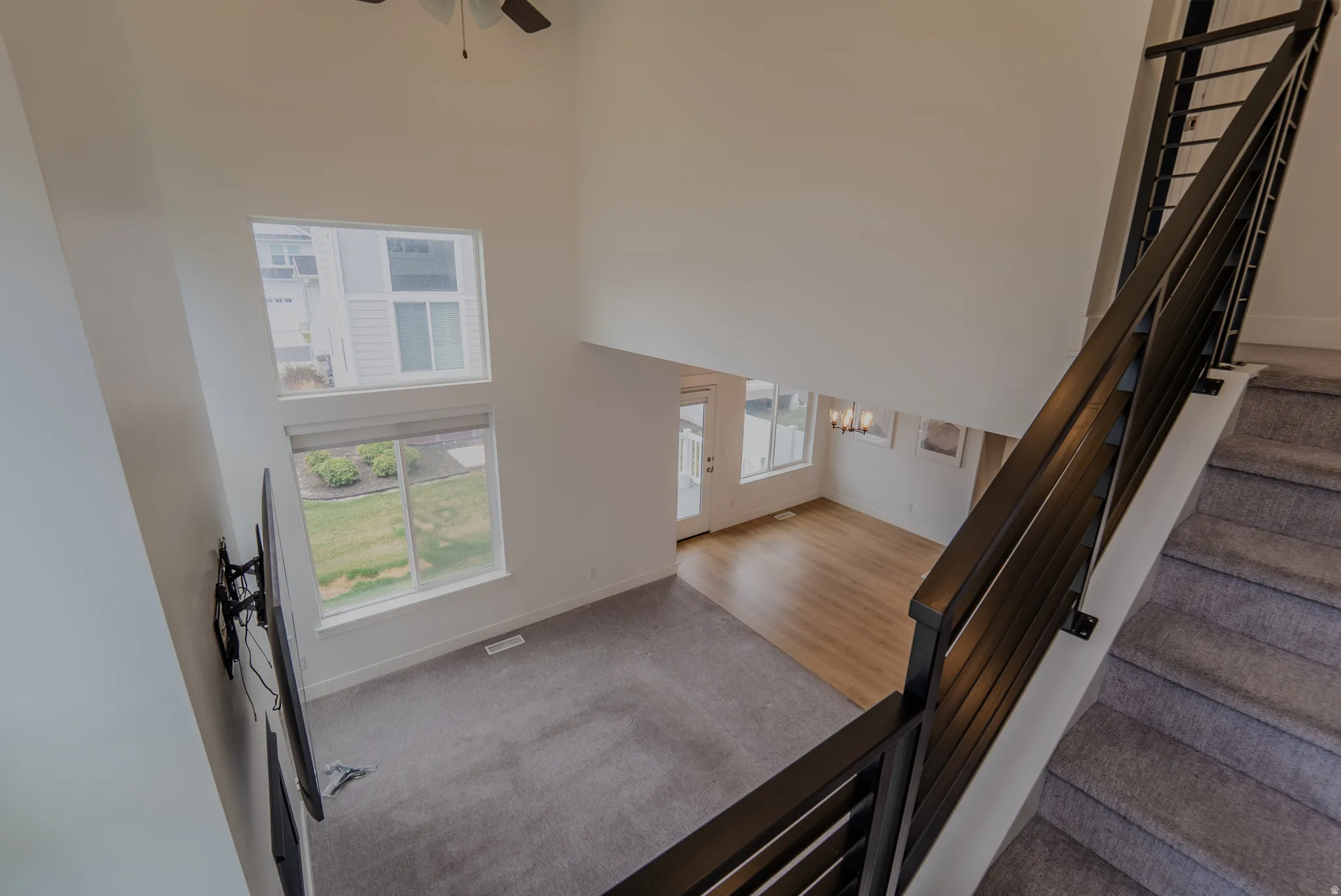 Two-story living area with high ceilings, multiple windows, wood-finish flooring, and a modern stair railing