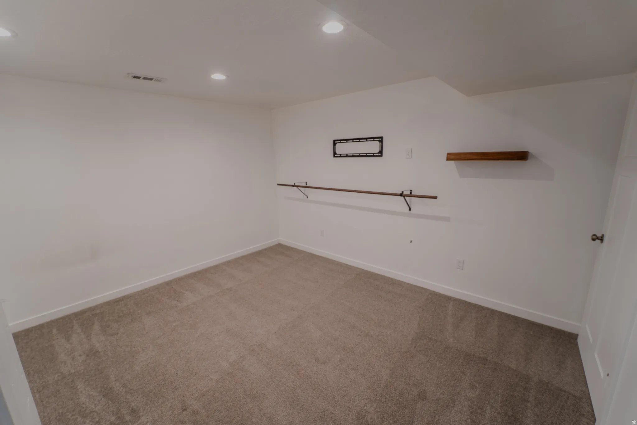 White-painted interior space featuring recessed lighting, a floating wood-finish shelf, and a garment rod