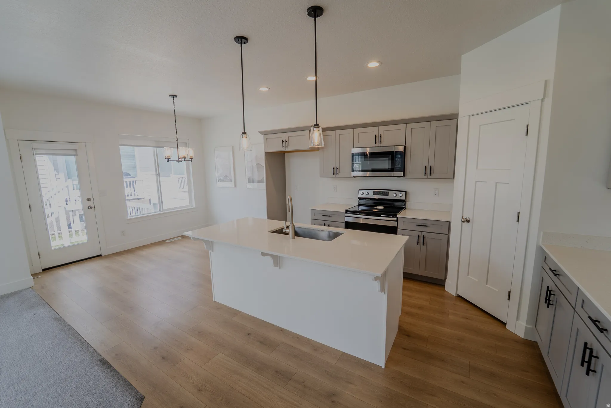 Open-concept kitchen and dining area featuring a central island with an integrated sink, stainless steel appliances, light gray cabinetry with dark hardware, and wood-finish flooring