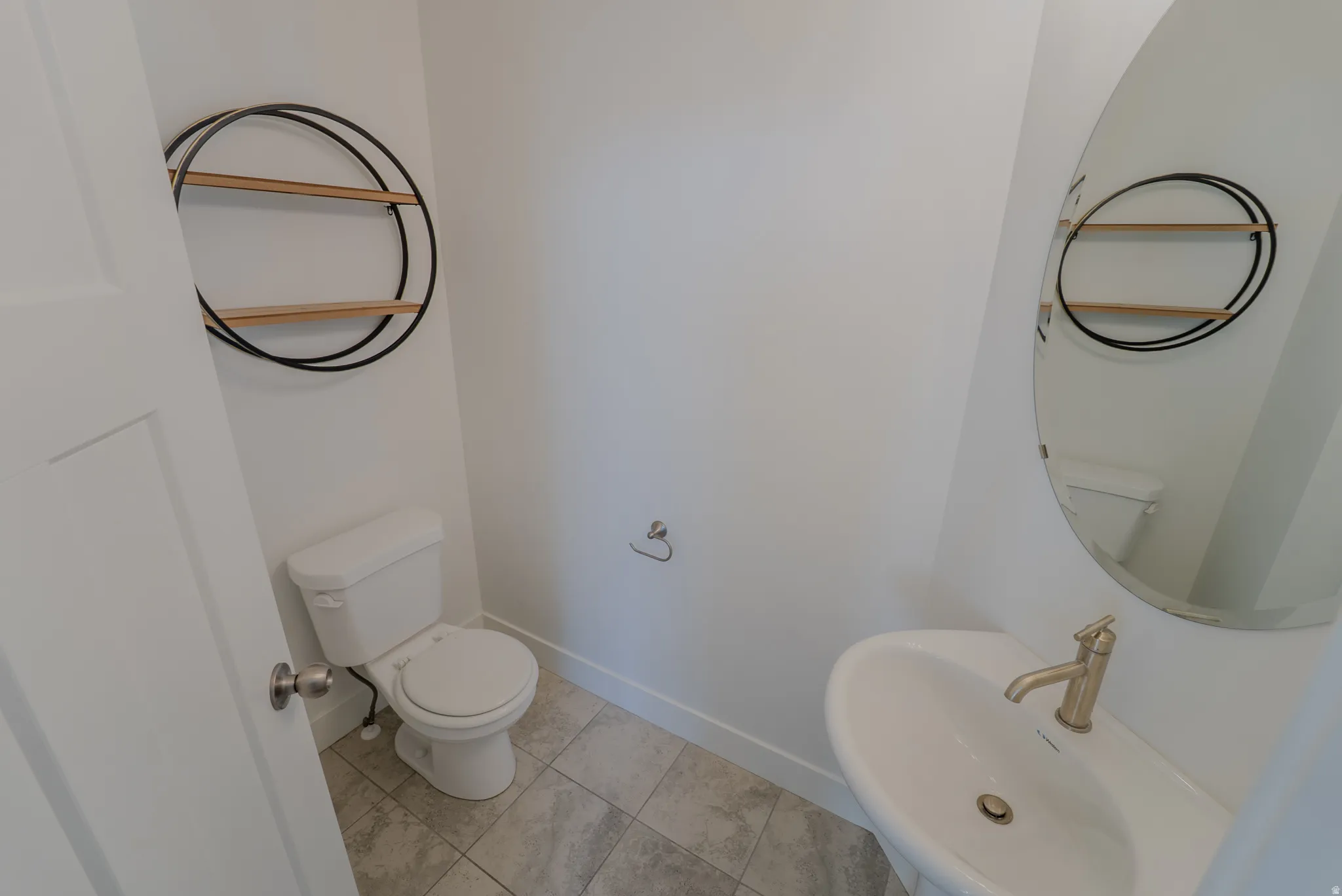 Pedestal sink with a champagne bronze faucet, complemented by a frameless oval mirror