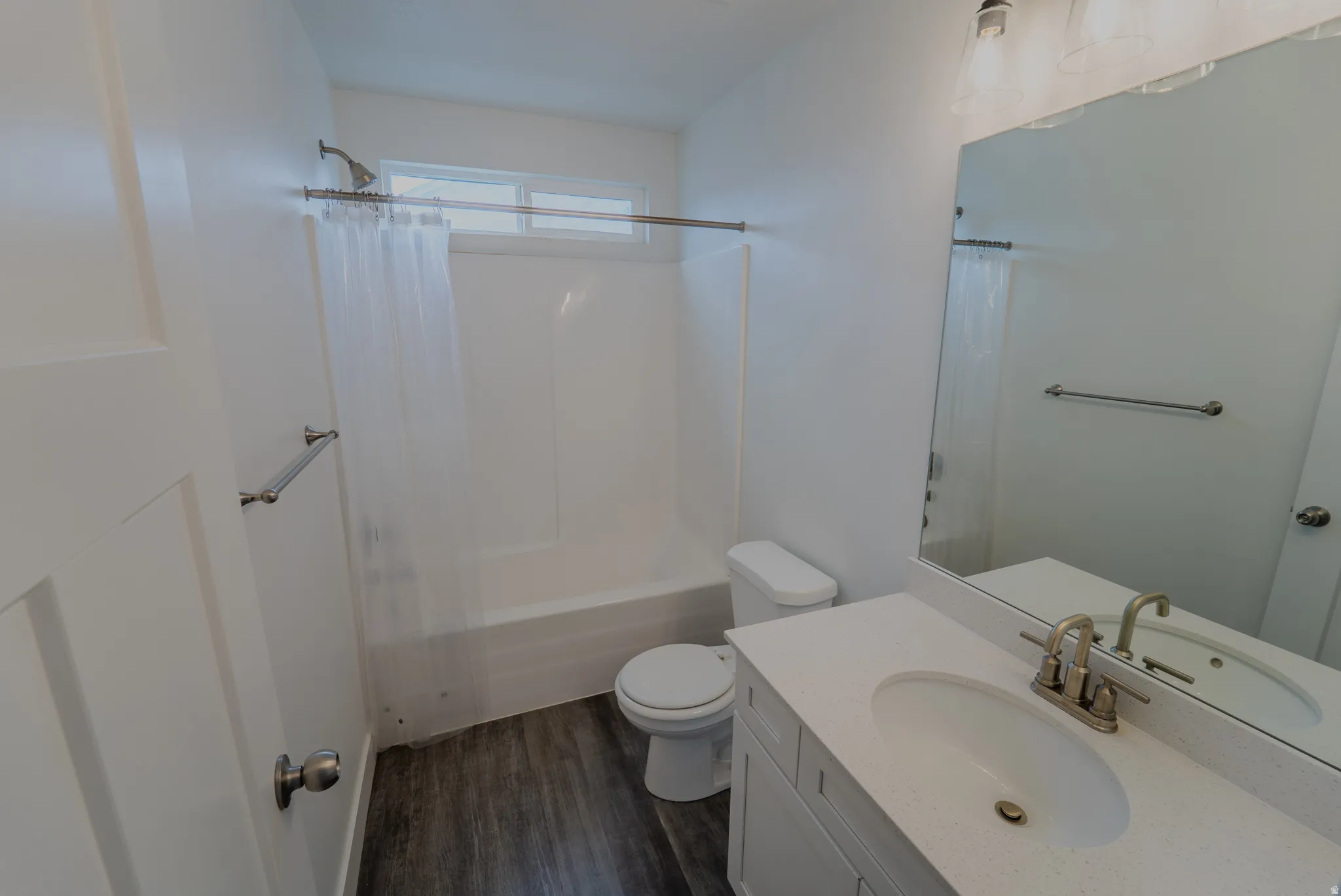 Bathroom featuring a vanity with an integrated sink and brushed nickel faucet, a large wall-mounted mirror, and a shower-tub combination with an overhead window