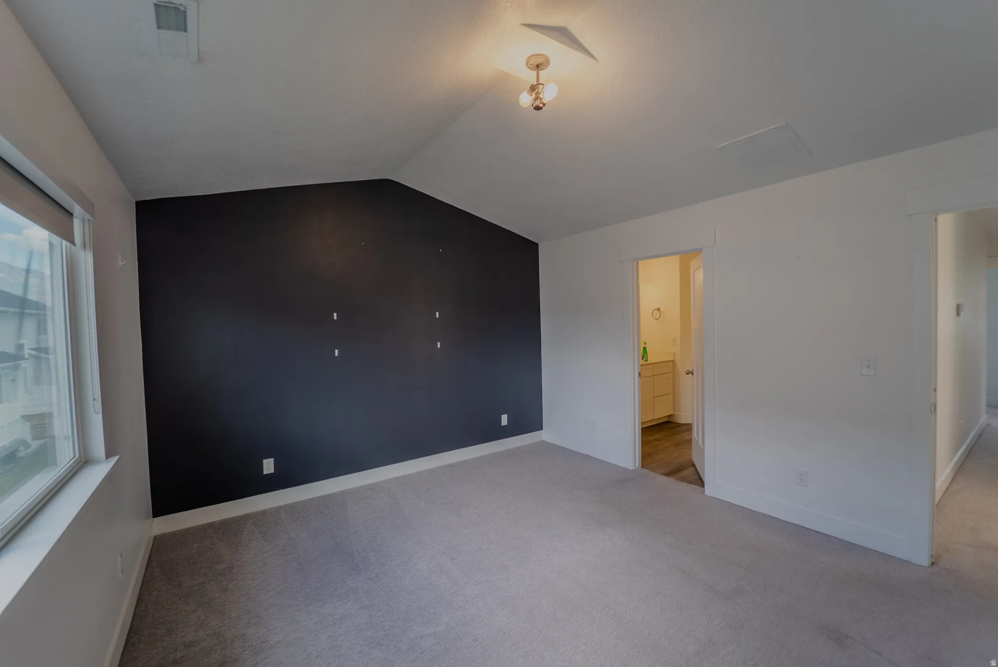 Spacious room featuring vaulted ceilings, a dark accent wall, and light grey carpet