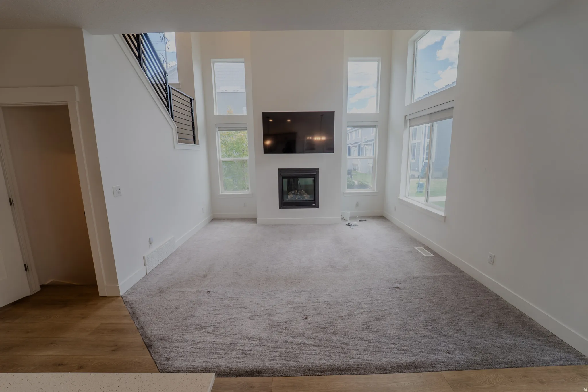 Double-height living area featuring a modern fireplace with a black surround, large rectangular windows, and a carpeted floor
