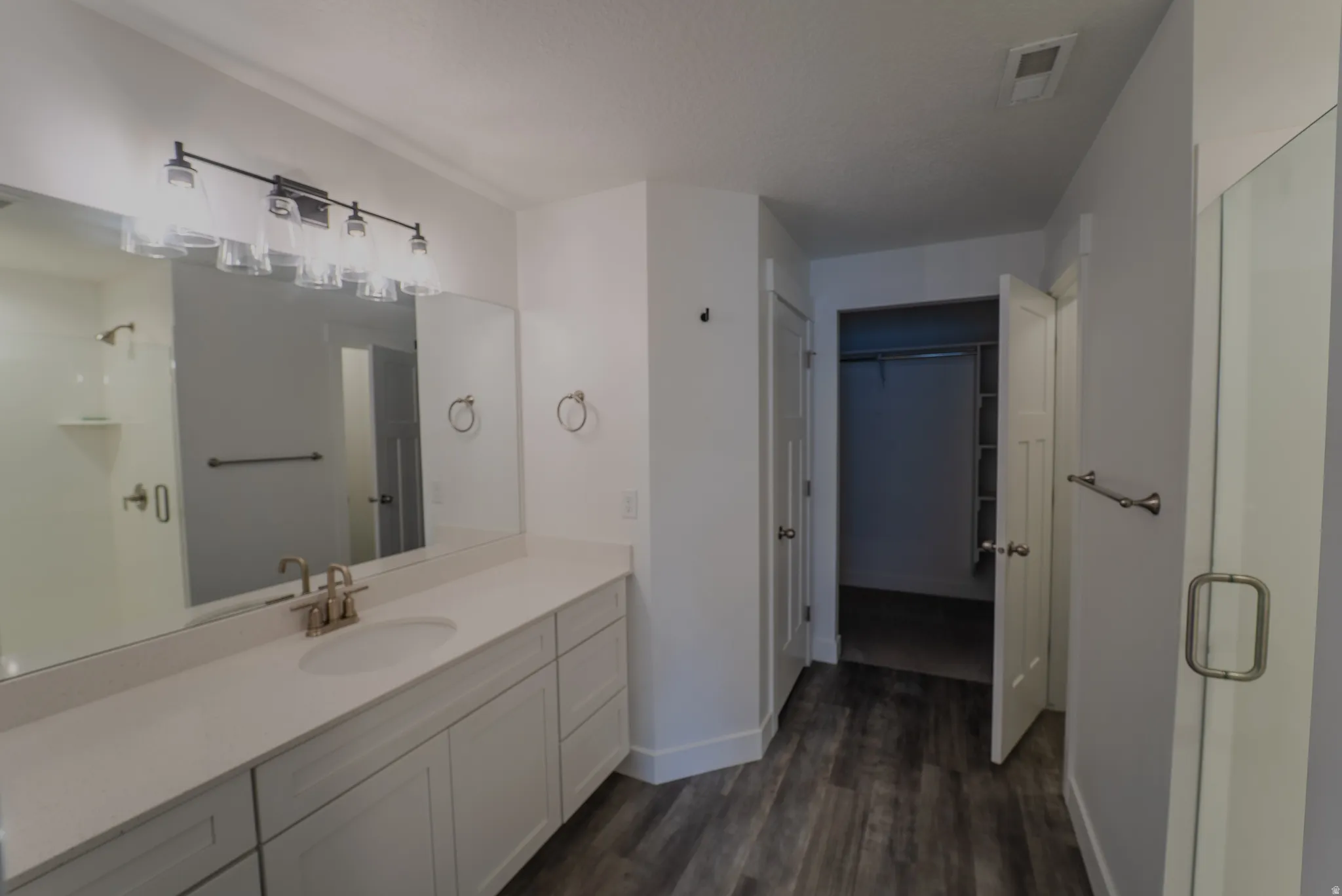 Bathroom featuring a dual vanity with a light-toned countertop, a large mirror, and wood-finish flooring
