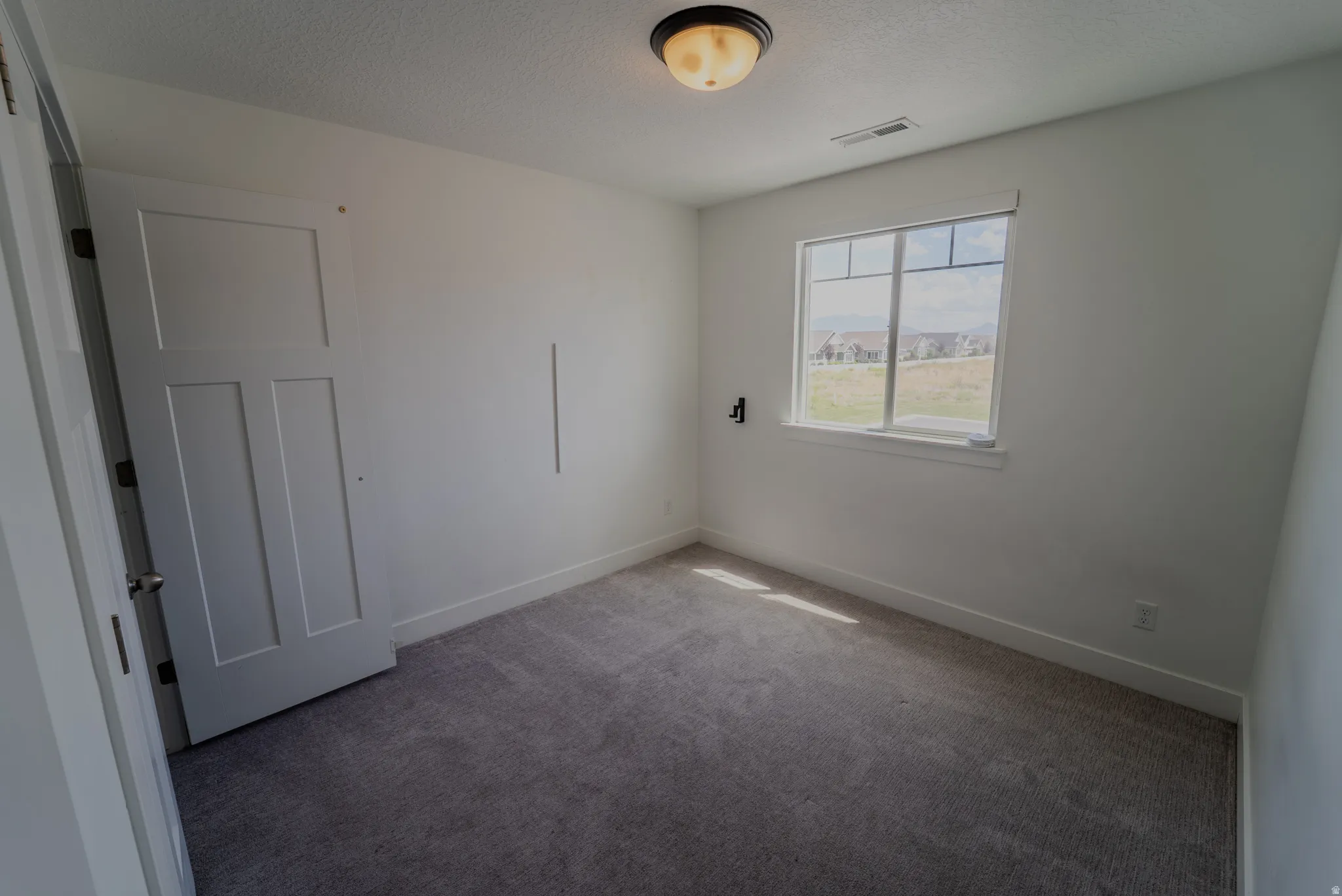 Interior room featuring a window with white trim, gray carpet, and a flush-mount ceiling light fixture