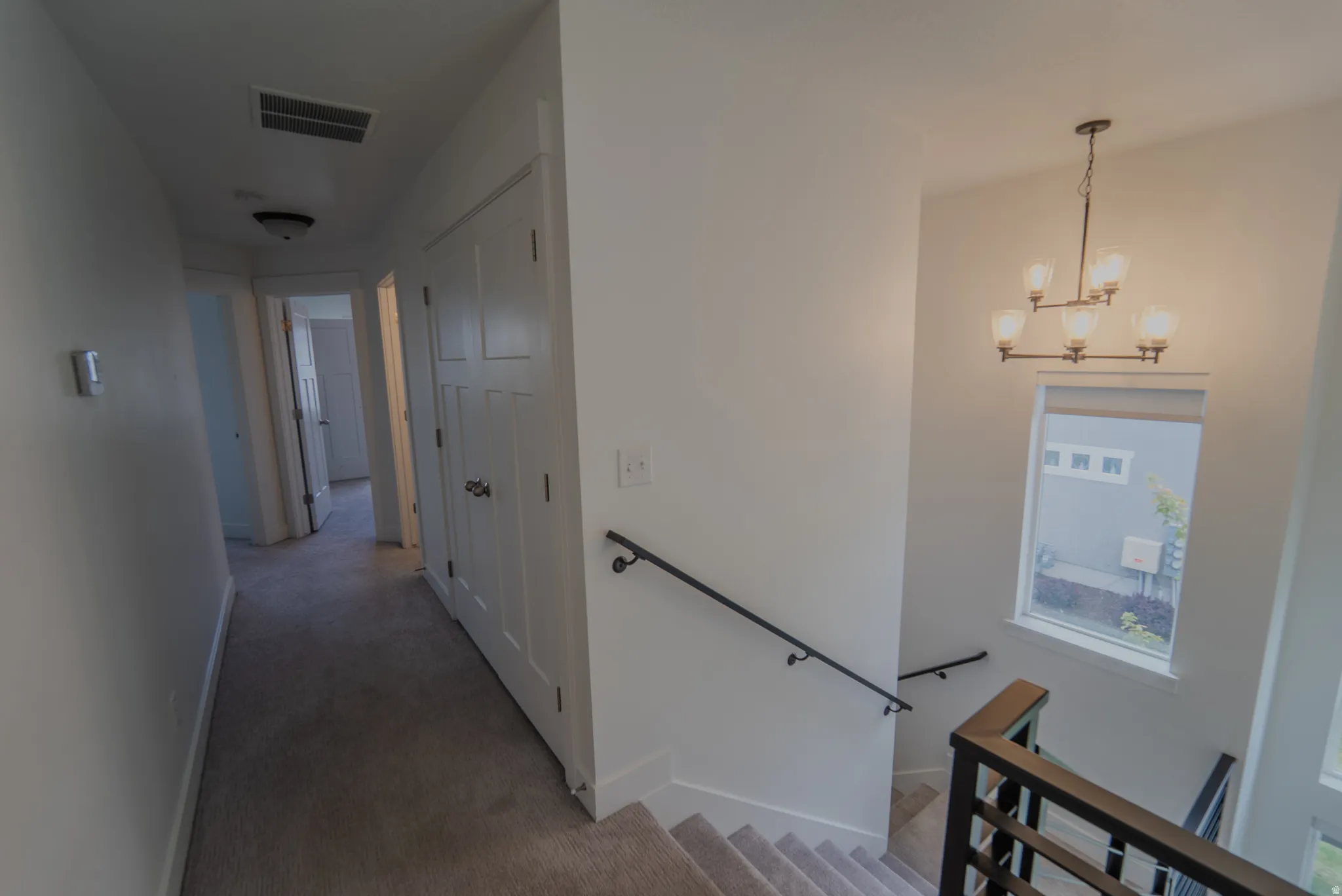 Carpeted hallway and staircase featuring a modern chandelier, white paneled doors, and contemporary black metal railings