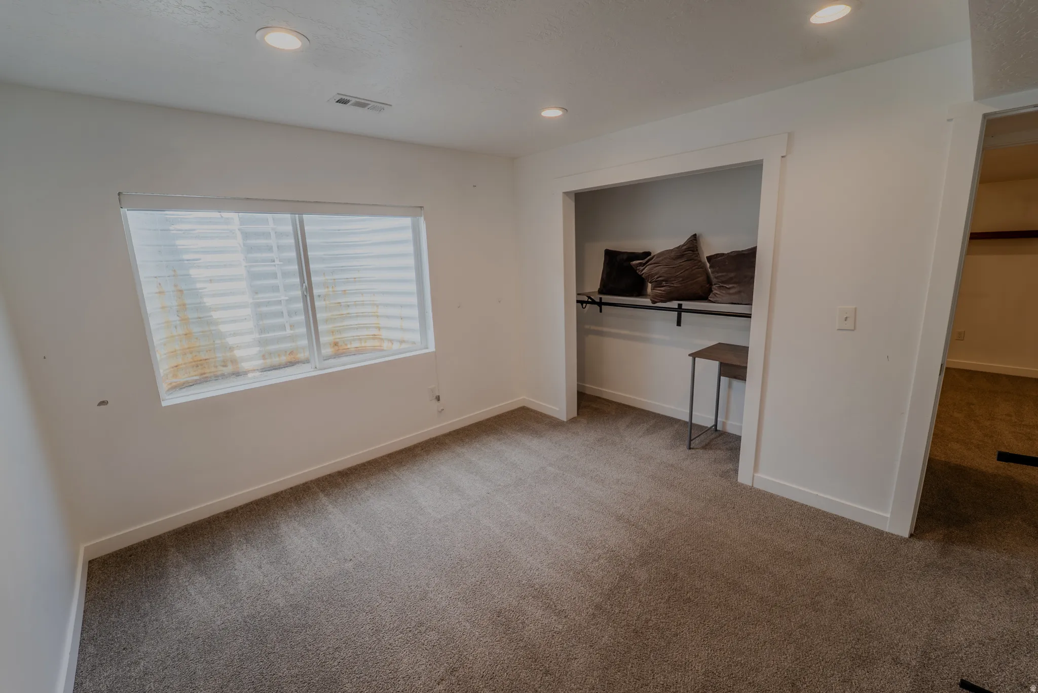 Carpeted room featuring recessed lighting, a window with horizontal blinds, and an open closet with a hanging rod