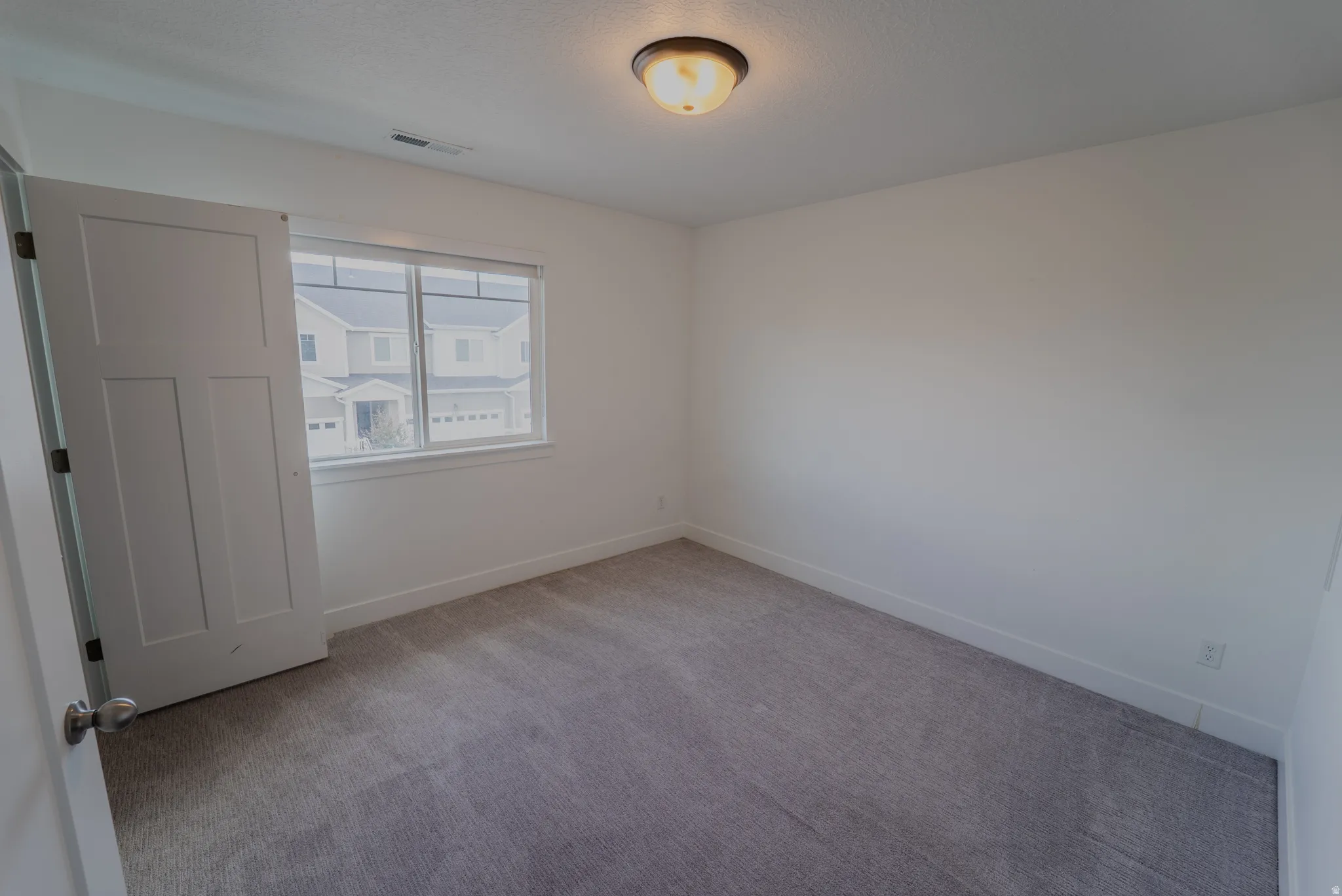 Neutral toned carpet flooring, white painted walls, and a multi-pane window