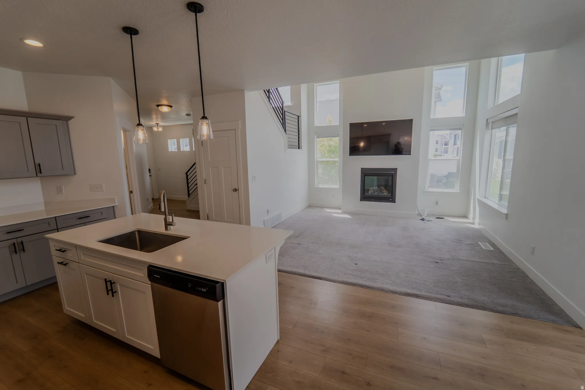 Kitchen island with a built-in stainless steel sink and dishwasher, wood-finish flooring, white cabinetry, gray upper cabinets, and a living area featuring a fireplace with a mounted television above