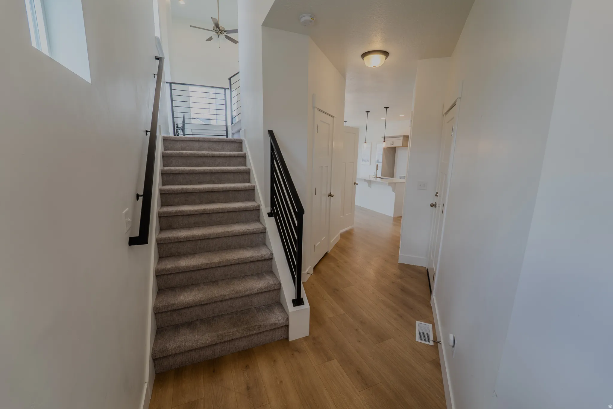 Entryway featuring wood-finish flooring, a carpeted staircase with modern black iron railings, and a flush-mount ceiling light