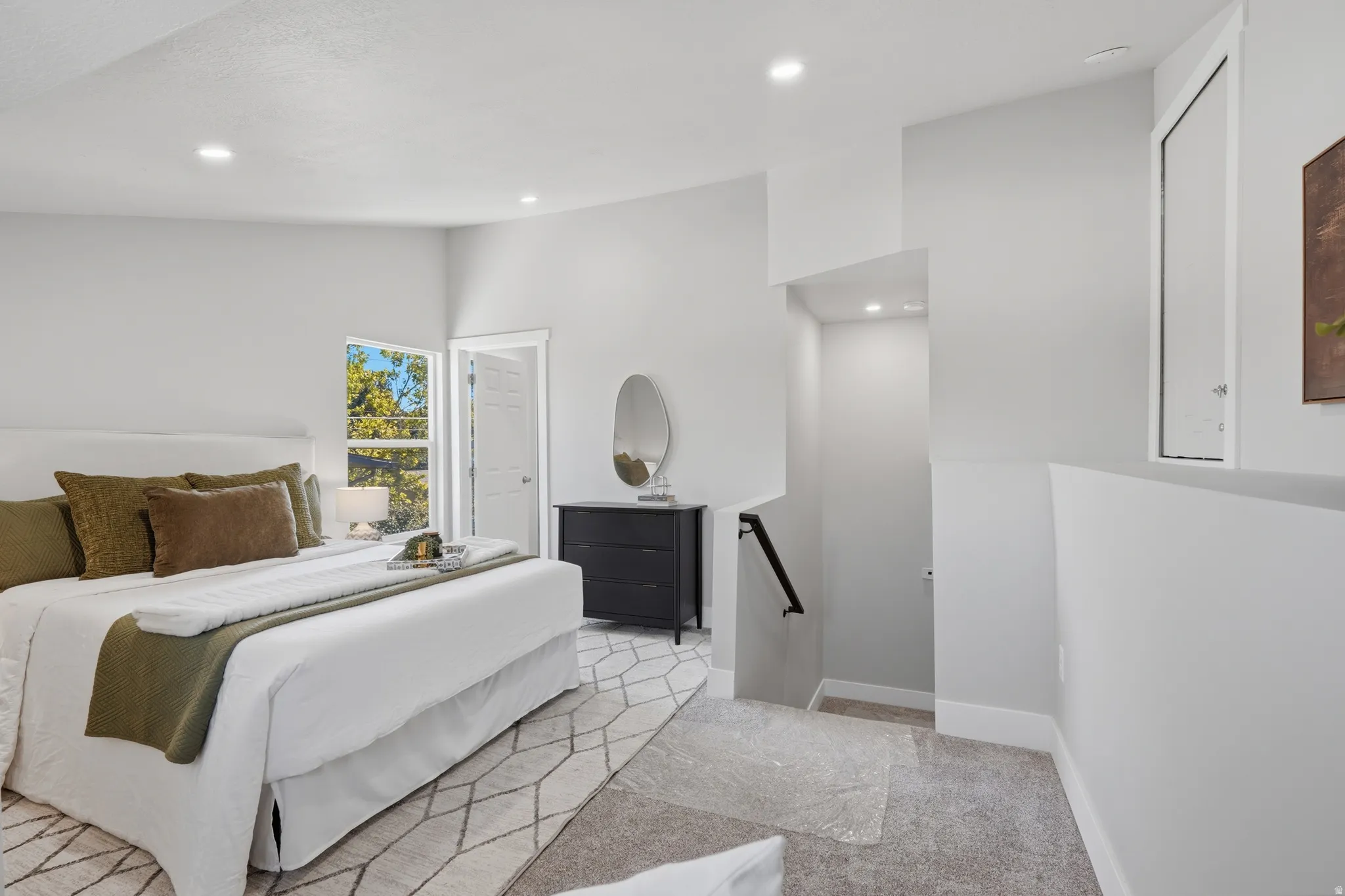 Bedroom featuring a window with exterior tree views, recessed lighting, and a partial staircase with a black handrail