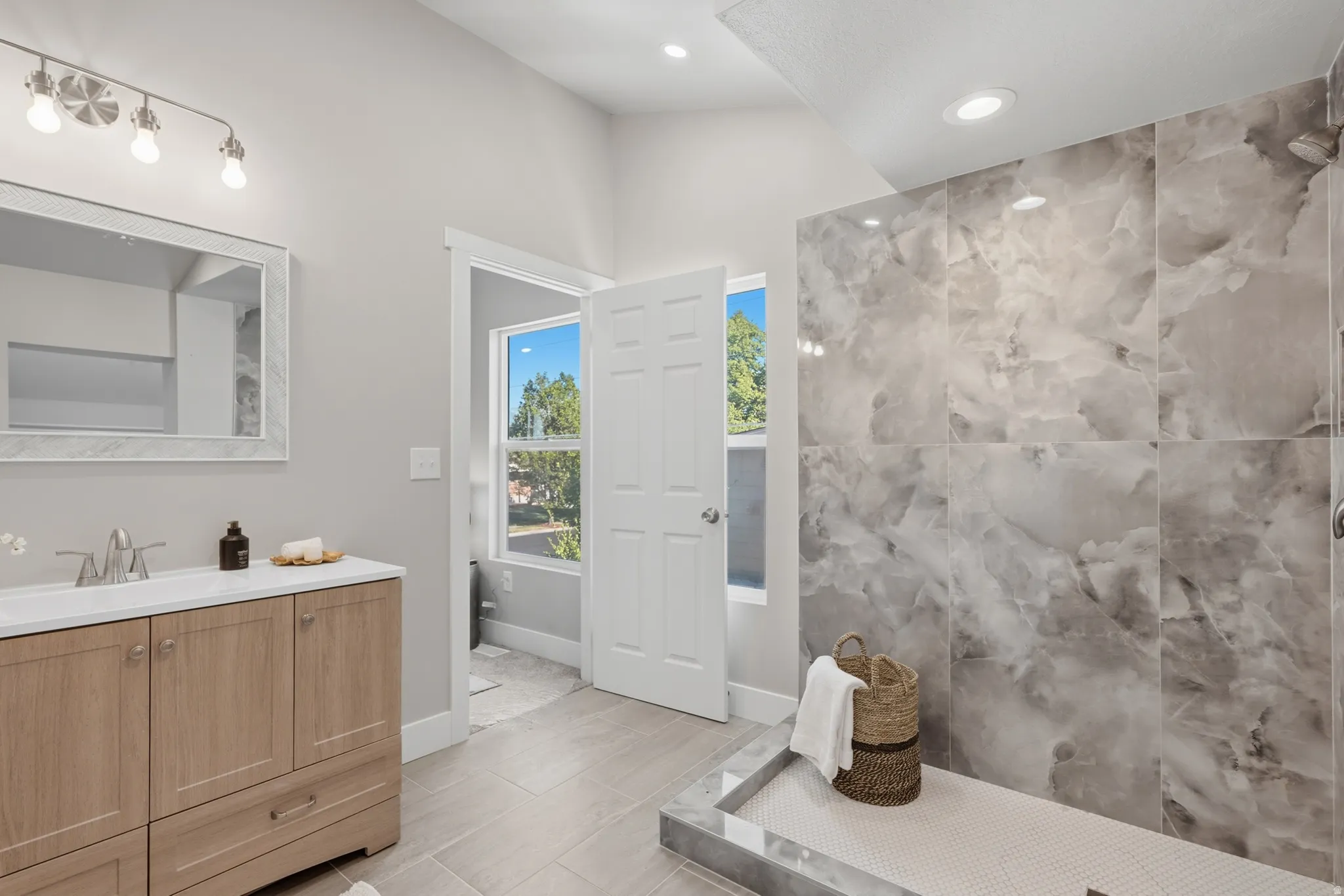 Spacious bathroom featuring a large walk-in shower with floor-to-ceiling marbled tile, wood-finish vanity with a single basin, brushed nickel hardware, and recessed lighting