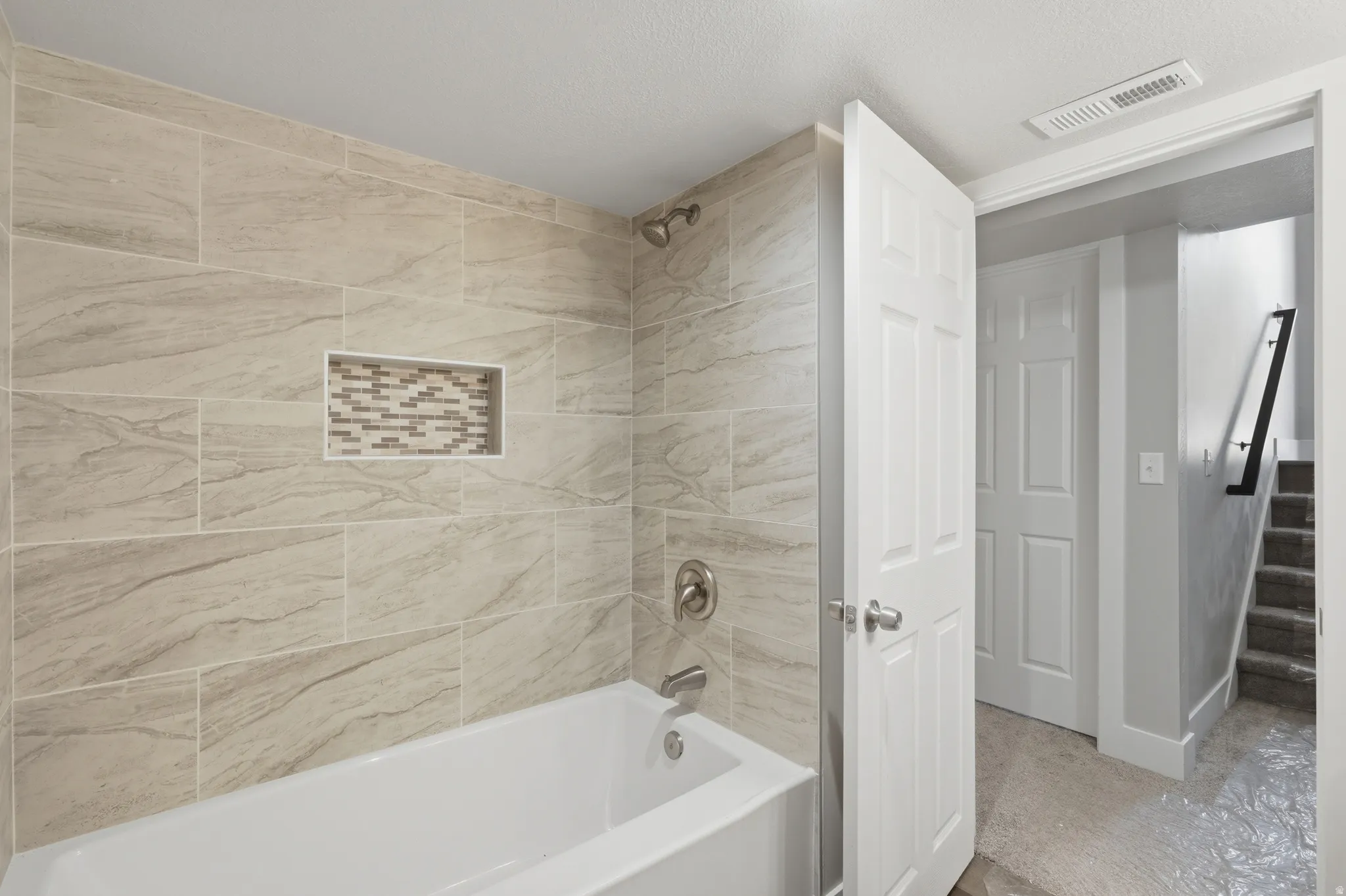 White bathtub with brushed nickel fixtures, surrounded by horizontal rectangular wall tiles