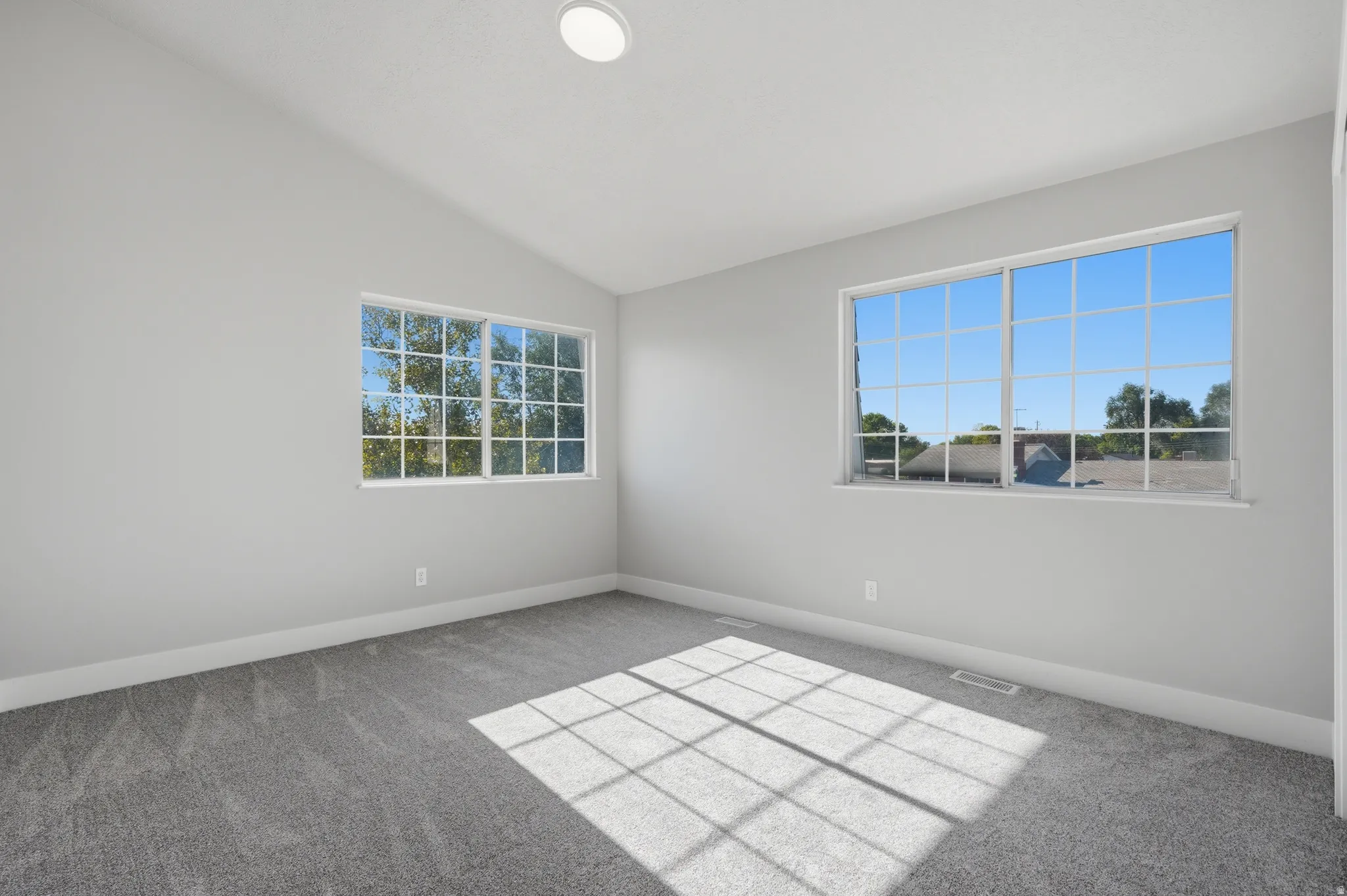 Bright interior room featuring a vaulted ceiling and two multi-pane windows