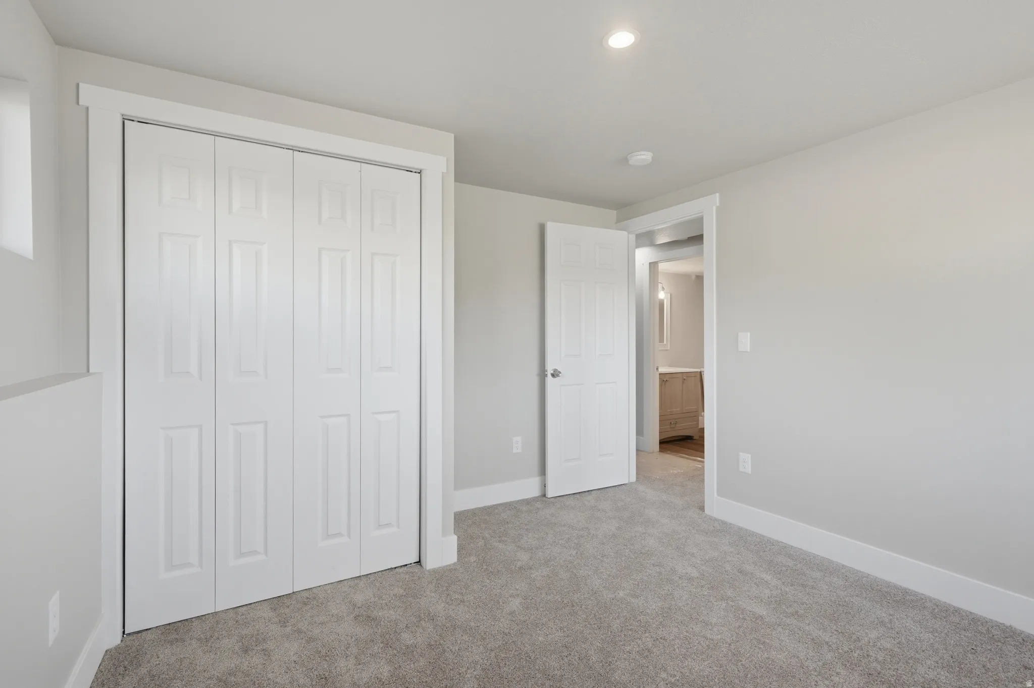 Carpeted room featuring a four-panel bi-fold closet, white trim, recessed lighting, and a window