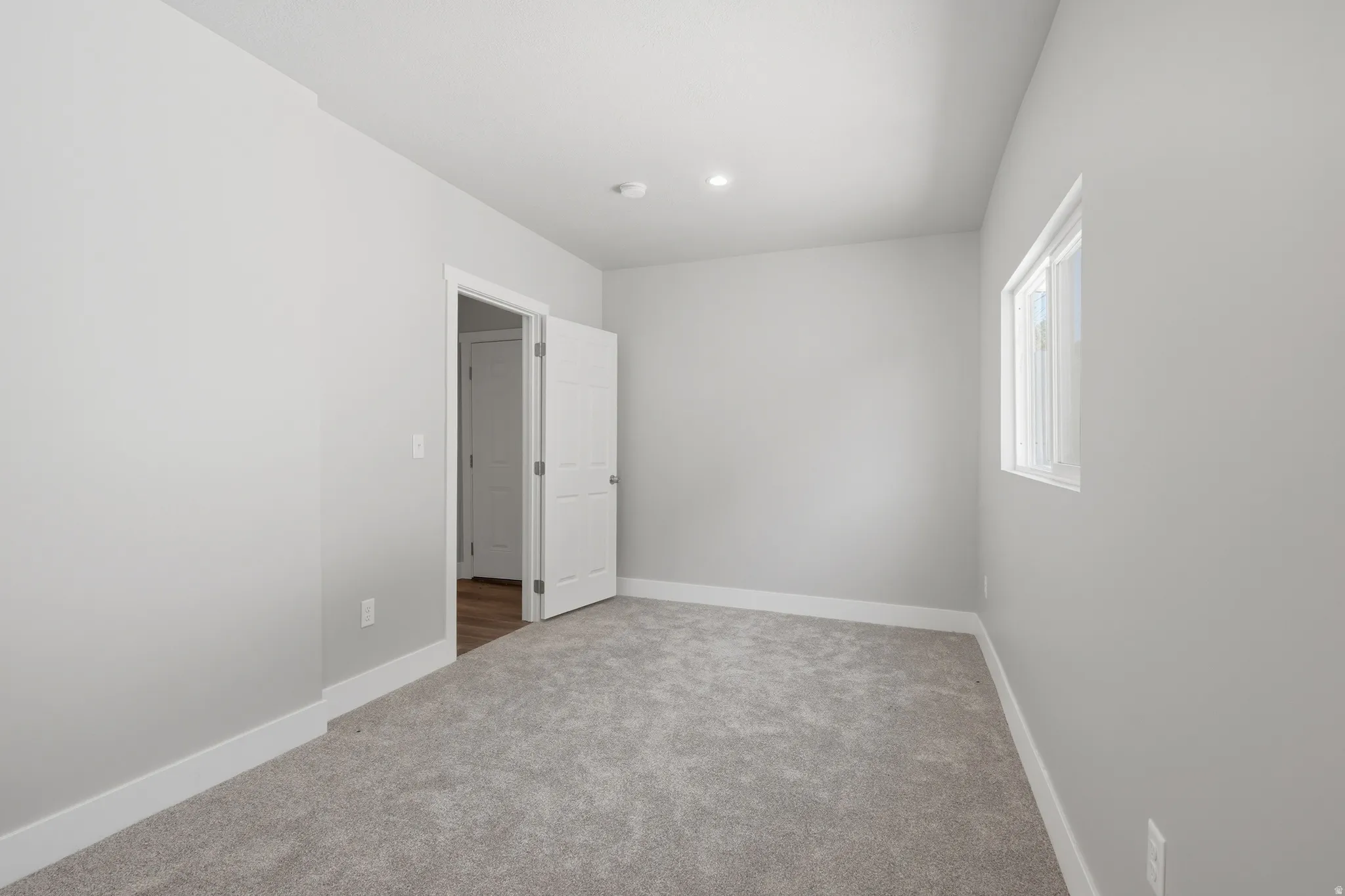 Carpeted room featuring a white interior door, a single window, recessed lighting, and light gray walls with white baseboards