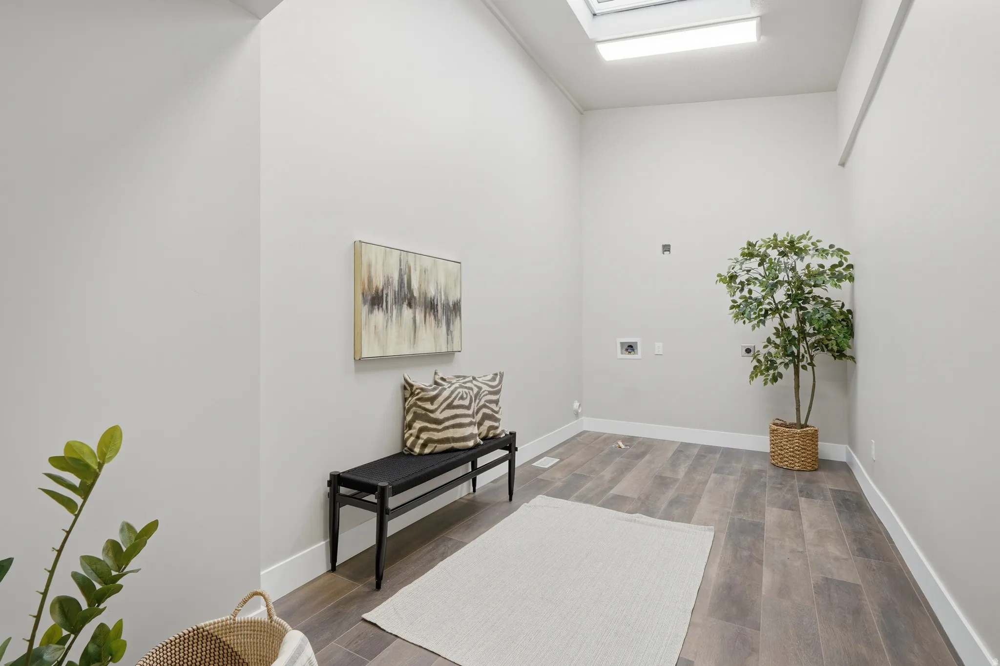 Utility room featuring wood-finish flooring, a skylight, white baseboards, and appliance hookups