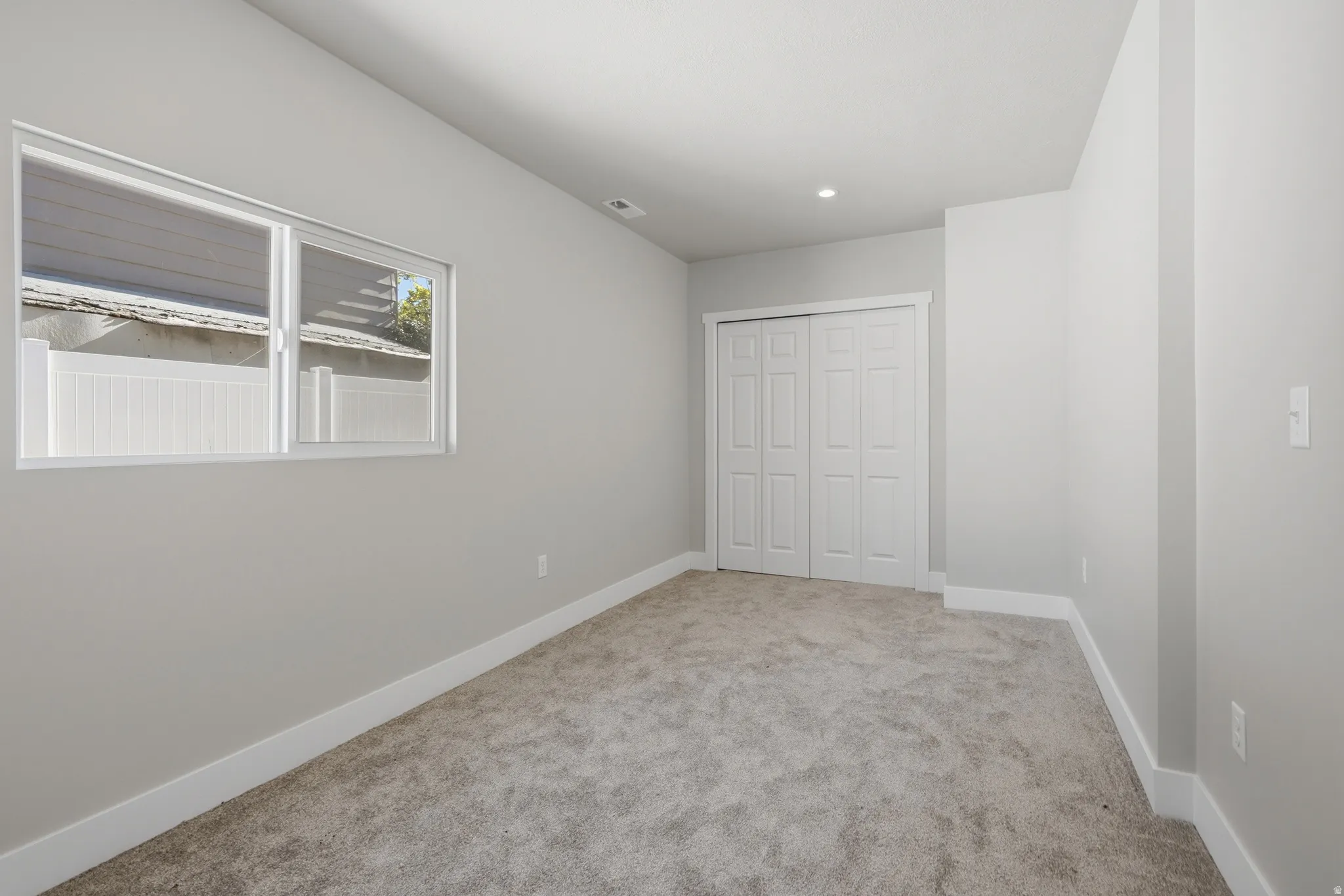 Carpeted room with a double-paned window, neutral wall paint, white trim, and a bi-fold closet door