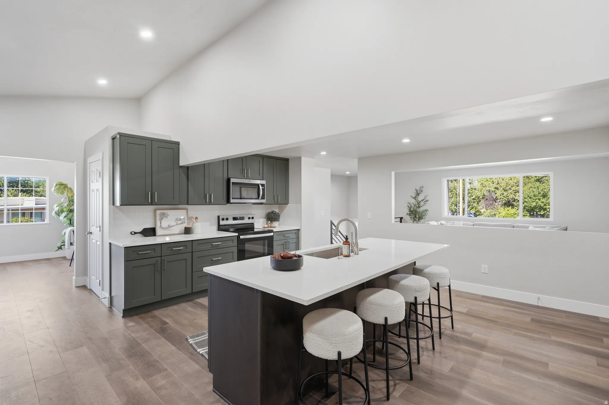 Modern kitchen featuring dark cabinetry, stainless steel appliances, a white subway tile backsplash, and a large center island with a white countertop and integrated sink