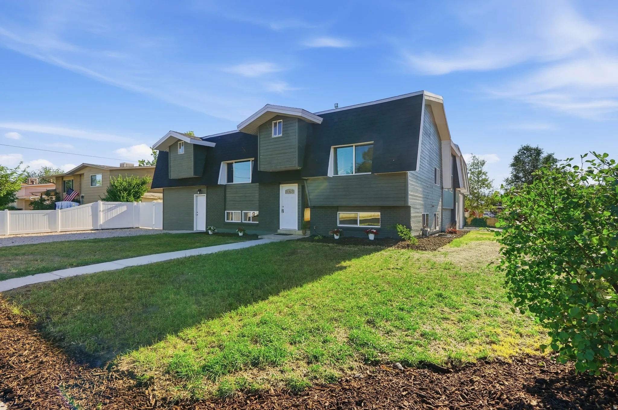 Gambrel roofline property featuring dark green siding, white entry door, and dormer windows