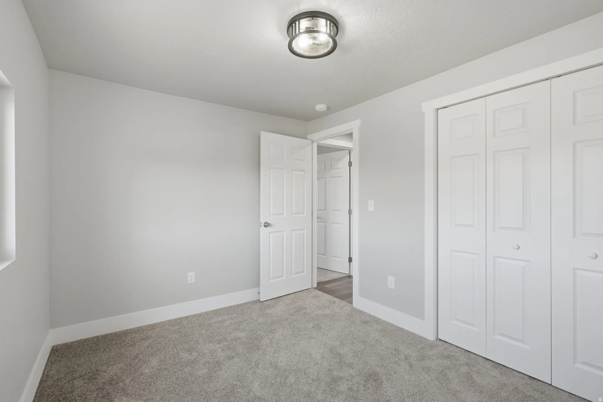 Neutral gray interior paint, gray carpet, white bi-fold closet doors, white baseboards, and a semi-flush mount ceiling light