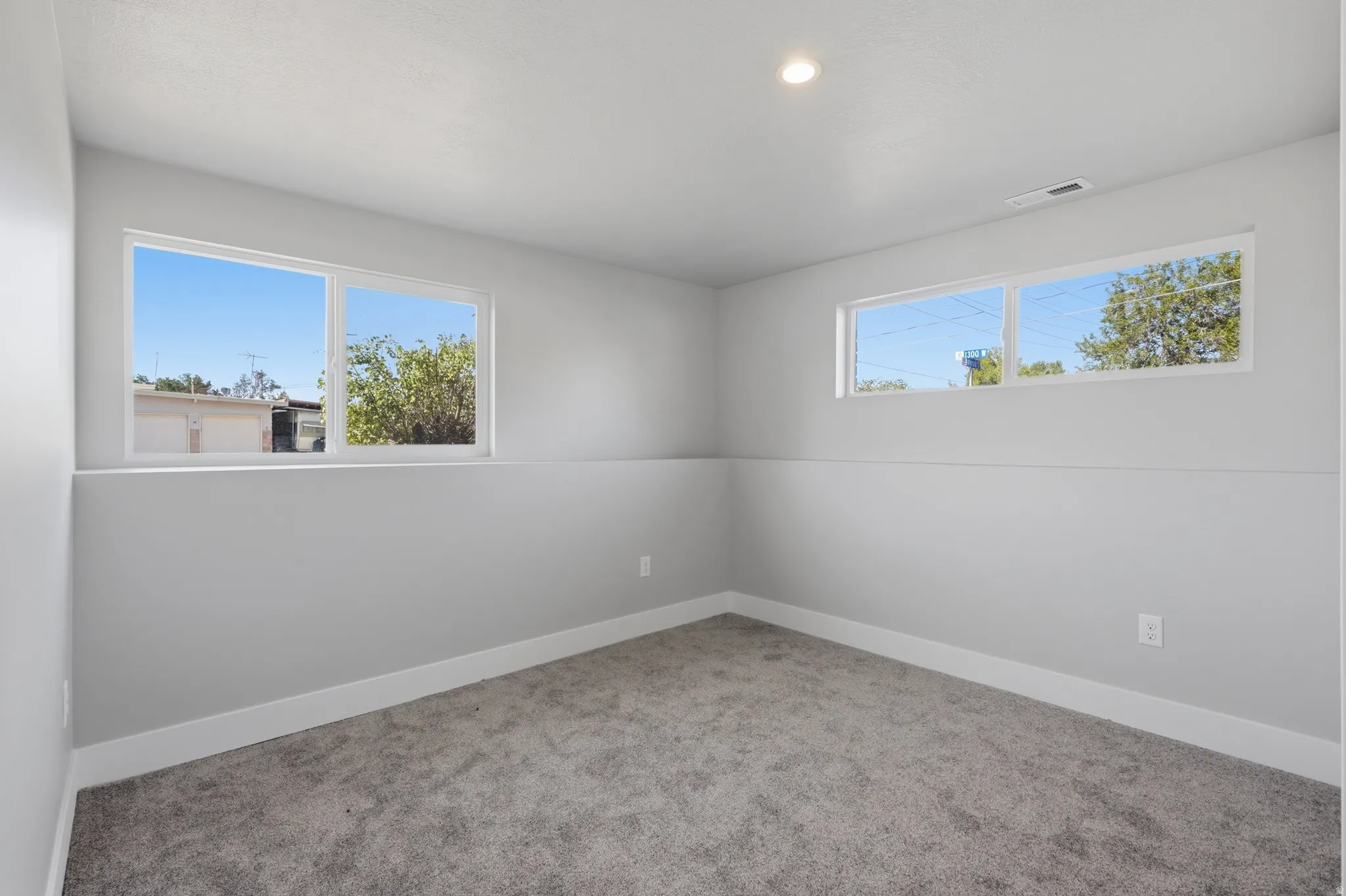 Room featuring light gray walls, white trim, gray carpet, and two egress windows
