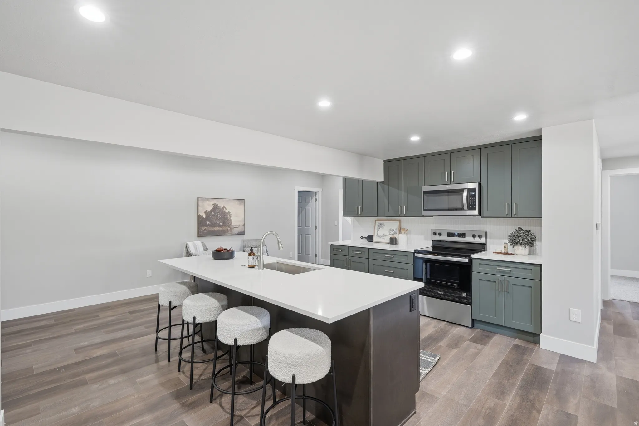 Kitchen featuring an expansive island with seating, white countertops, sleek green cabinetry, stainless steel appliances, and wood-finish flooring