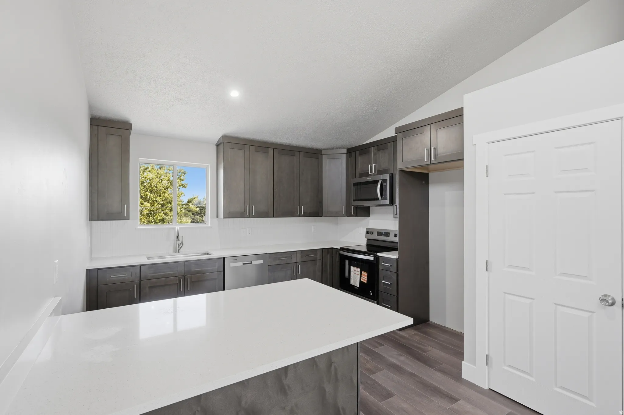 Kitchen featuring a central island with a solid surface countertop, wood-finish flooring, recessed lighting, and sloped ceilings
