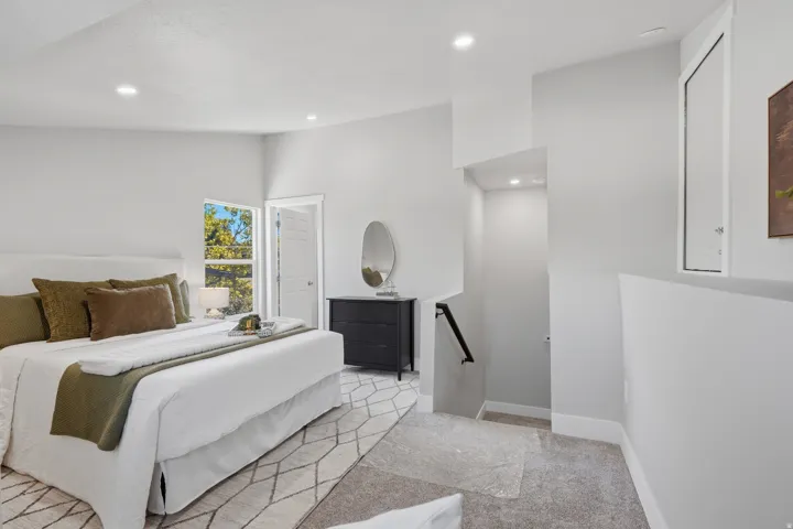 Bedroom featuring a window with exterior tree views, recessed lighting, and a partial staircase with a black handrail