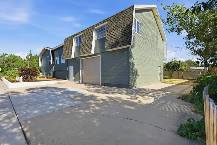 Multi-level exterior with dormer windows, a large roll-up garage door, concrete driveways, and a raised planter bed