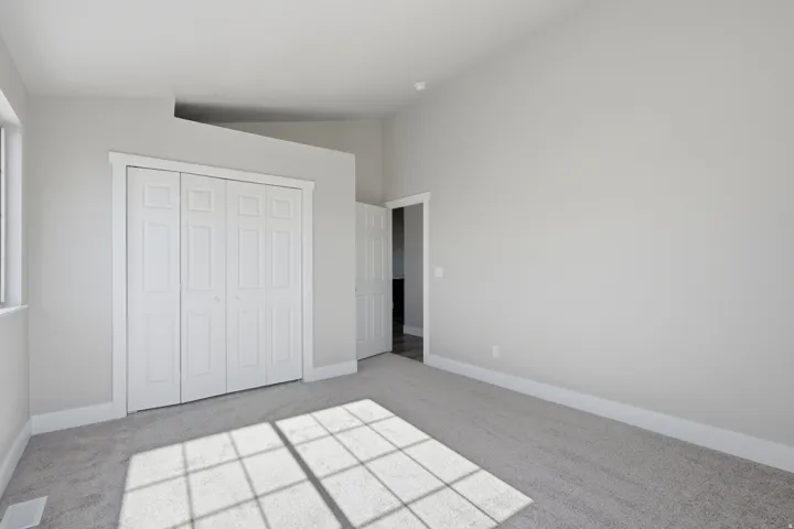 Spacious room featuring light gray wall paint, light gray carpet, white bi-fold closet doors, white baseboards, and a vaulted ceiling