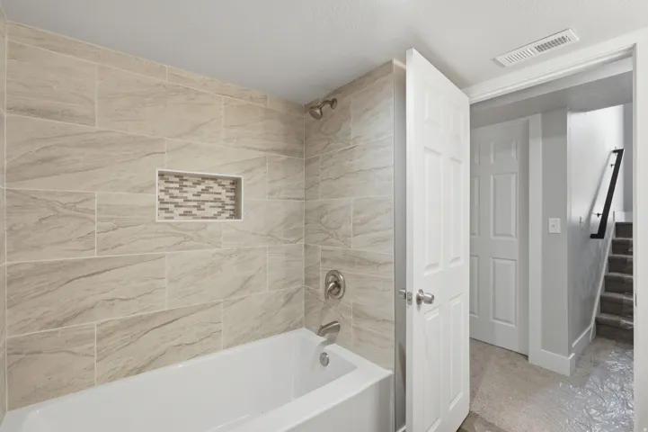 White bathtub with brushed nickel fixtures, surrounded by horizontal rectangular wall tiles