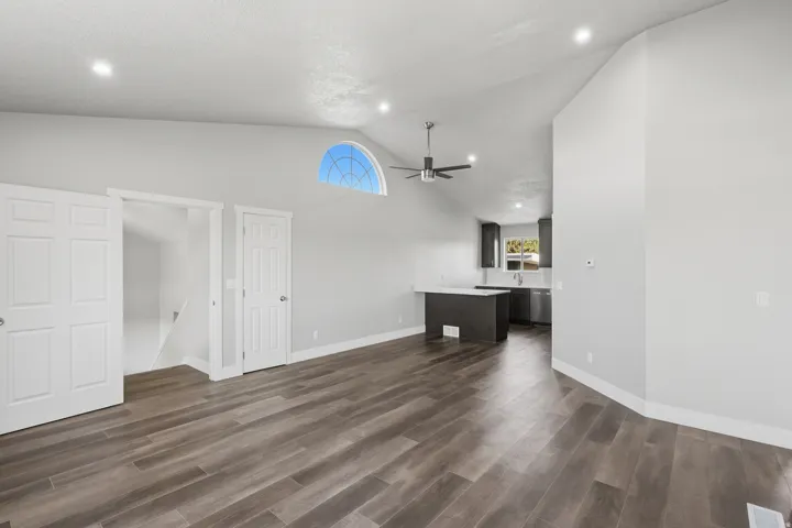 Vaulted ceiling living area featuring wood-finish flooring, a contemporary ceiling fan, and recessed lighting