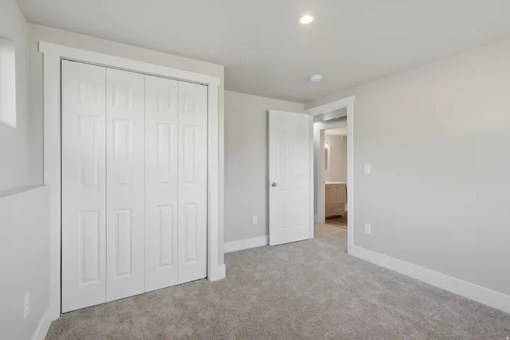 Carpeted room featuring a four-panel bi-fold closet, white trim, recessed lighting, and a window