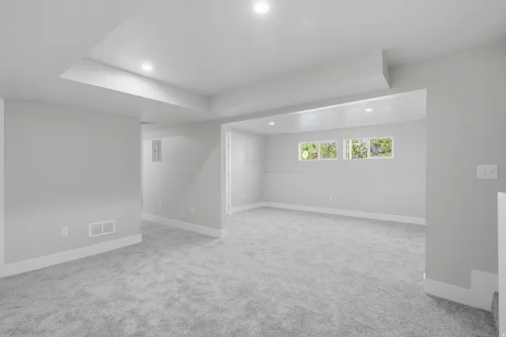 Spacious interior room featuring light gray carpeting, white baseboards, recessed ceiling lighting, and multiple windows