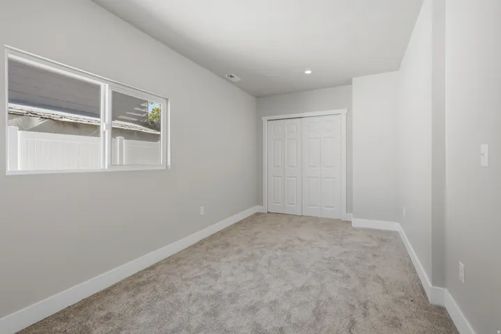 Carpeted room with a double-paned window, neutral wall paint, white trim, and a bi-fold closet door