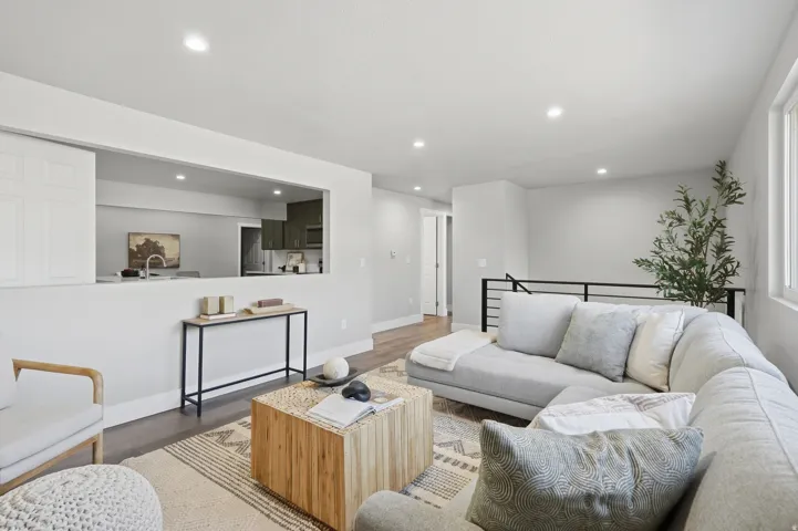 Open-concept living space featuring wood-finish flooring, recessed lighting, a pass-through window to the kitchen, and a staircase with a black metal railing