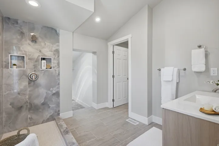Spacious bathroom featuring a walk-in shower with large format gray marble-look tile and integrated shelving
