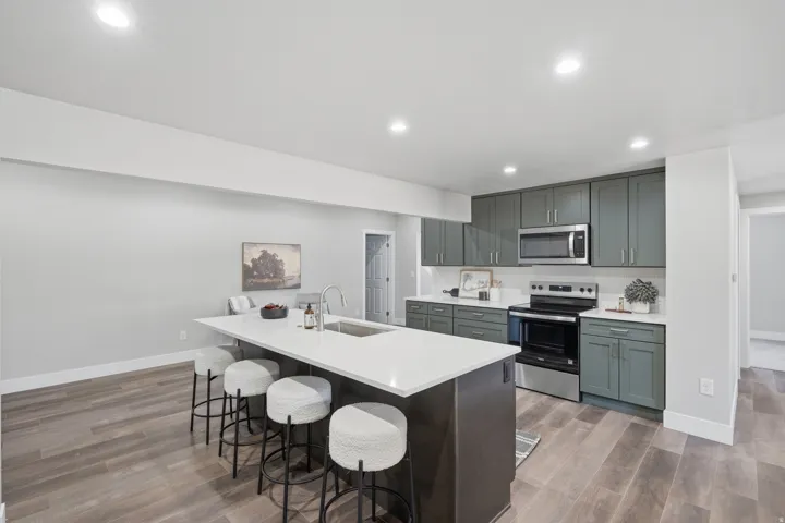 Kitchen featuring an expansive island with seating, white countertops, sleek green cabinetry, stainless steel appliances, and wood-finish flooring