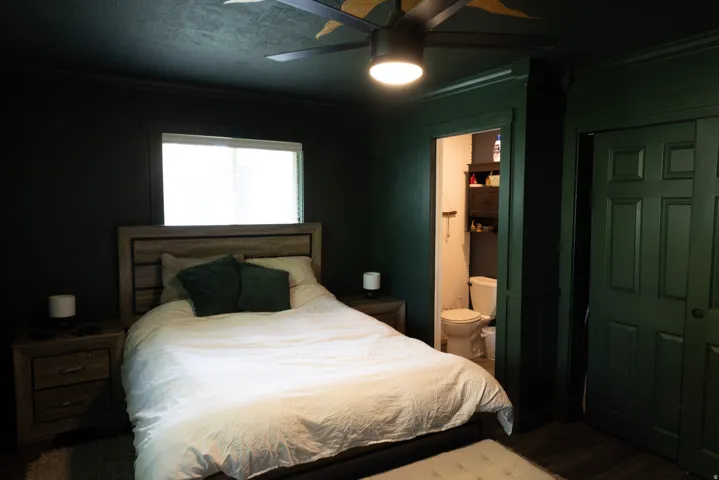 Bedroom featuring dark paneled walls, a ceiling fan with integrated lighting, a window with blinds, and wood-finish flooring