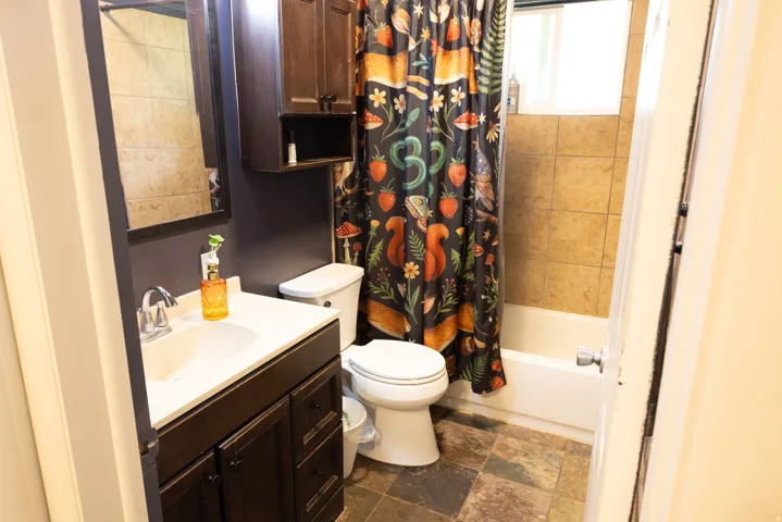 Bathroom featuring a single vanity with a white countertop and dark wood-finish cabinetry, a toilet, and a bathtub with tile surround