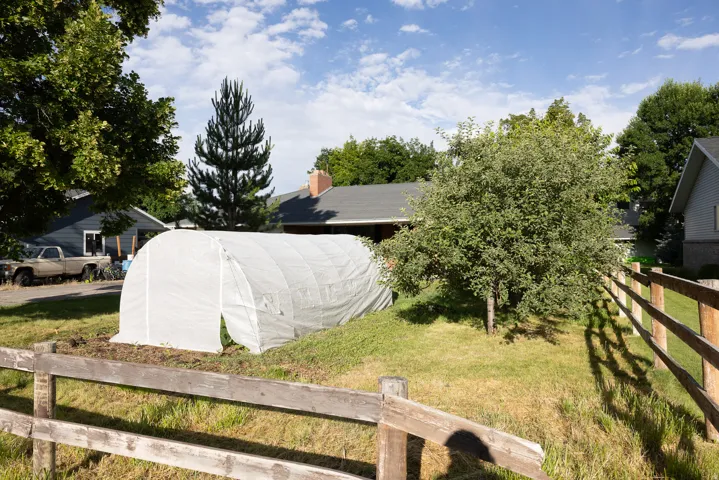 Expansive outdoor space featuring a covered hoop house, mature deciduous trees, and a split-rail fence