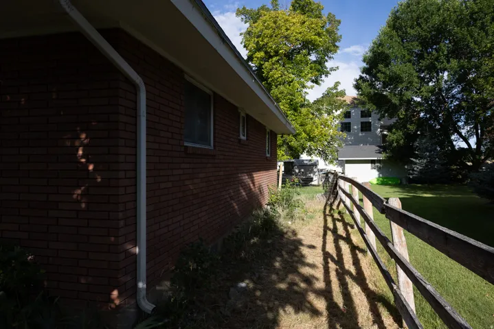 Brick exterior with white downspouts and fascia, featuring a wood rail fence bordering a grass lawn