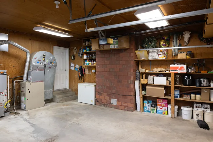 Concrete flooring garage with plywood-paneled walls and ceiling, featuring fluorescent lighting fixtures