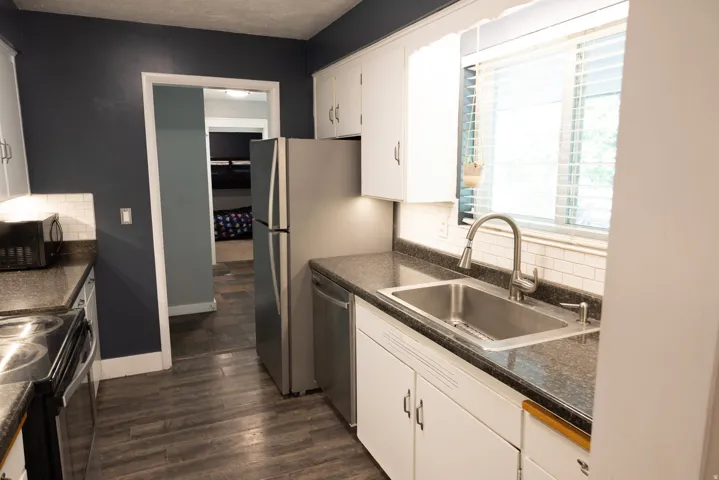 Kitchen featuring white cabinetry, dark countertops, wood-finish flooring, stainless steel appliances, and a white subway tile backsplash