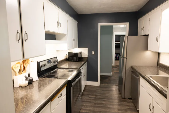 Galley kitchen featuring white cabinetry, dark speckled countertops, and wood-finish flooring